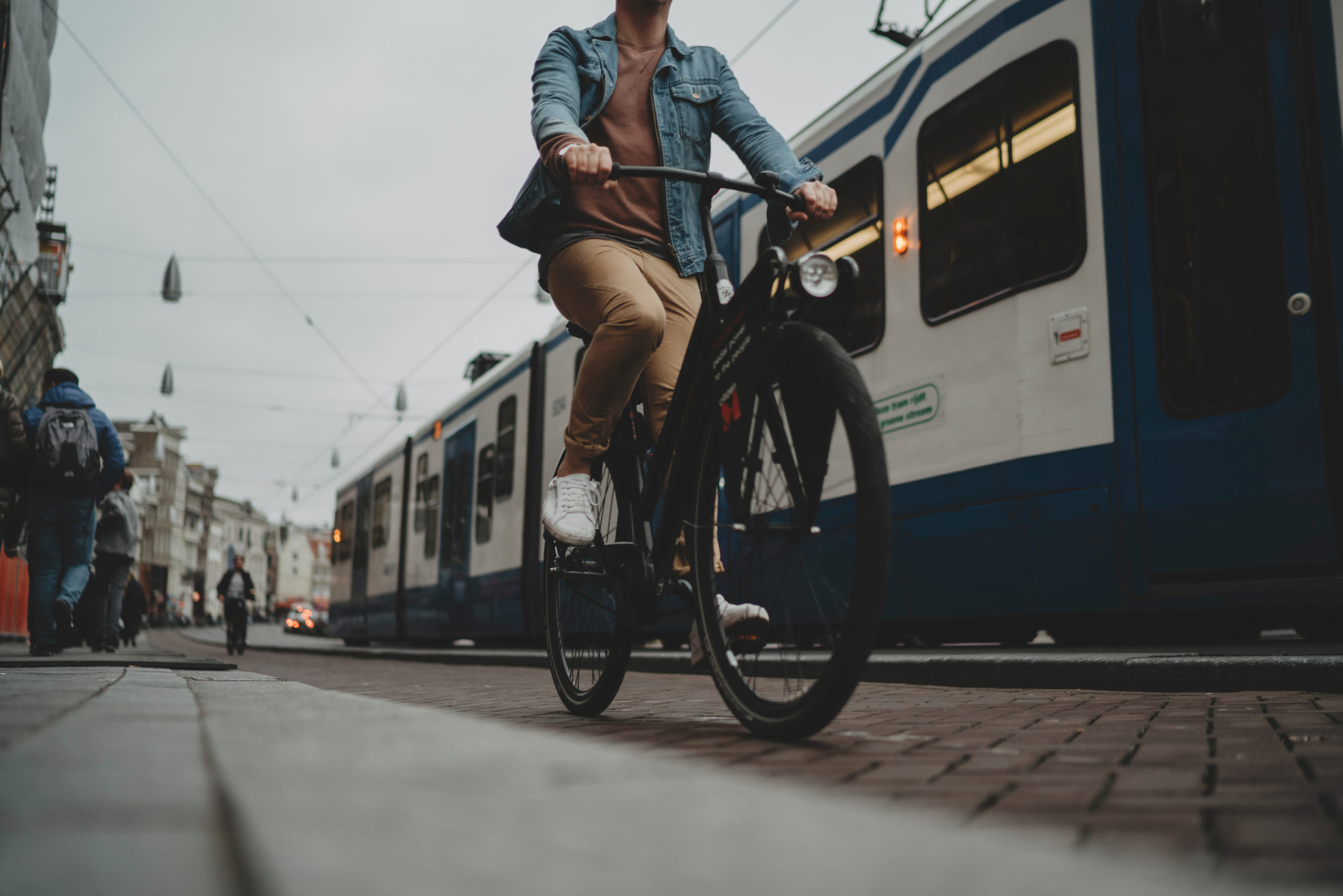 Young hipster guy driving modern black bicycle on cycle track, tram on the background