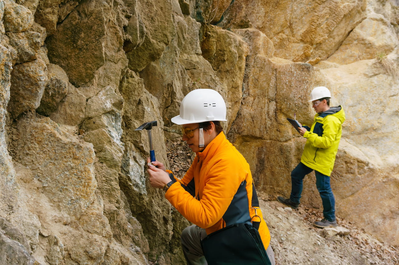 Two workers using hammers to secure rows of materials into a mountain wall, engaged in construction or mining work.