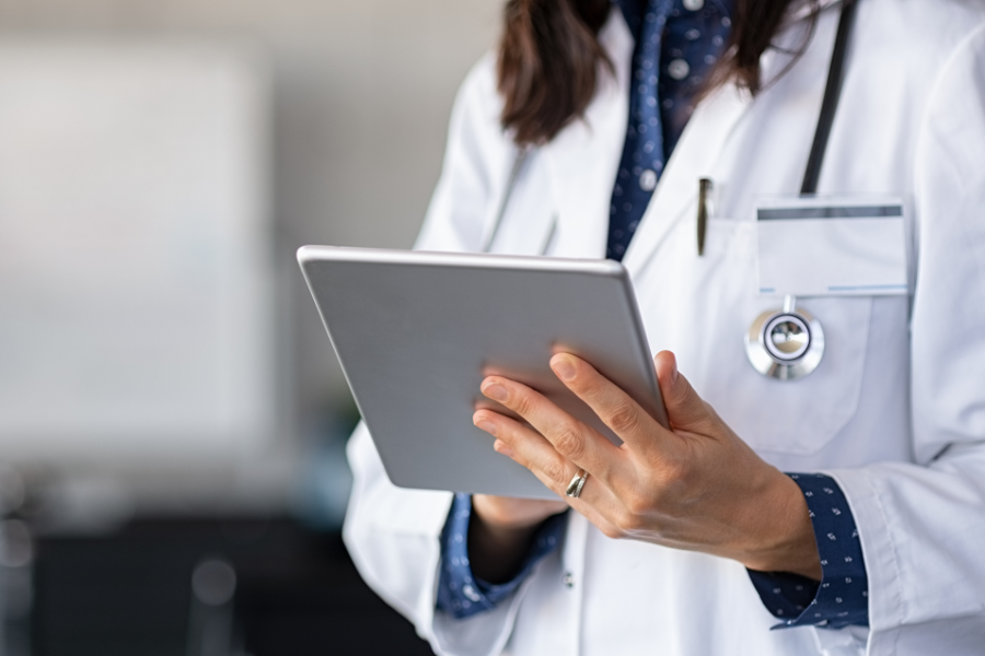 A doctor writing notes on a tablet, documenting patient information in a medical setting.