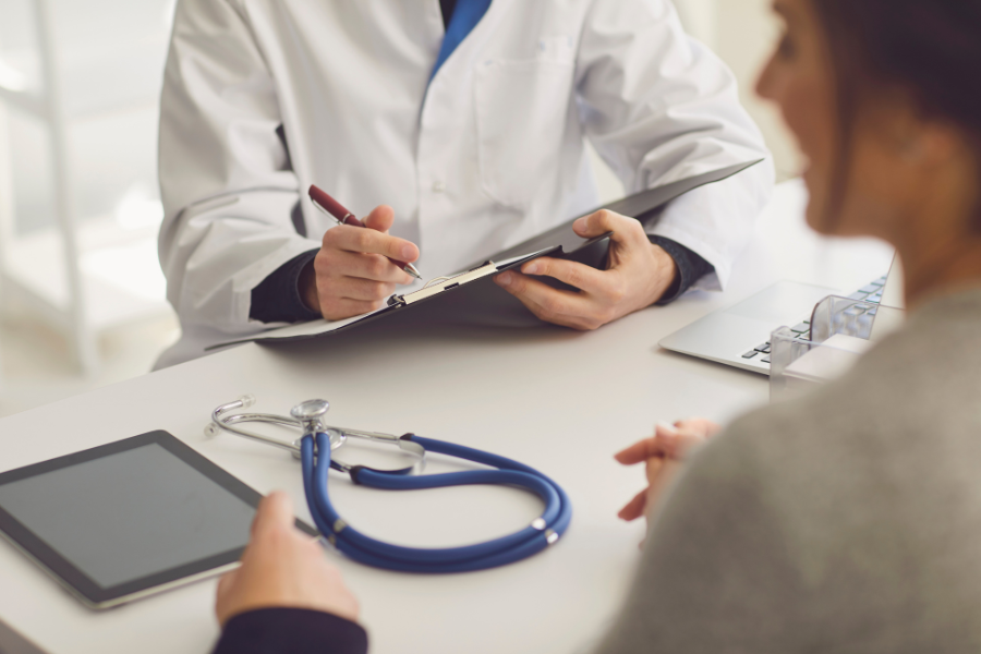 A doctor writing notes on a clipboard, documenting patient information in a medical setting.