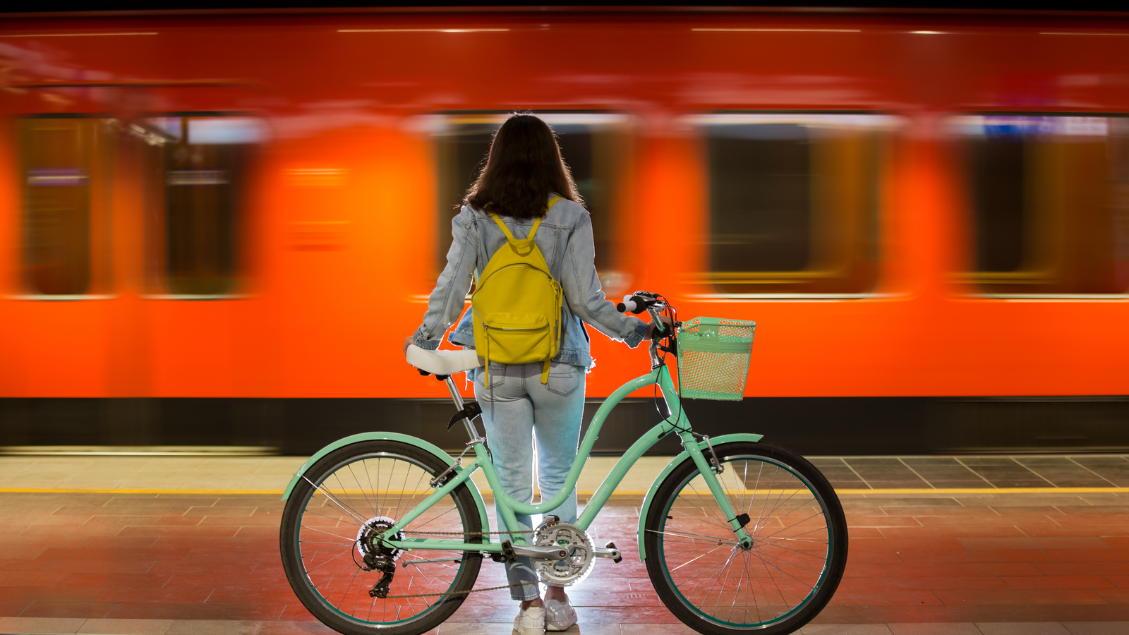 A woman holding a bicycle in front of a metro station, symbolizing sustainable transportation or urban mobility.