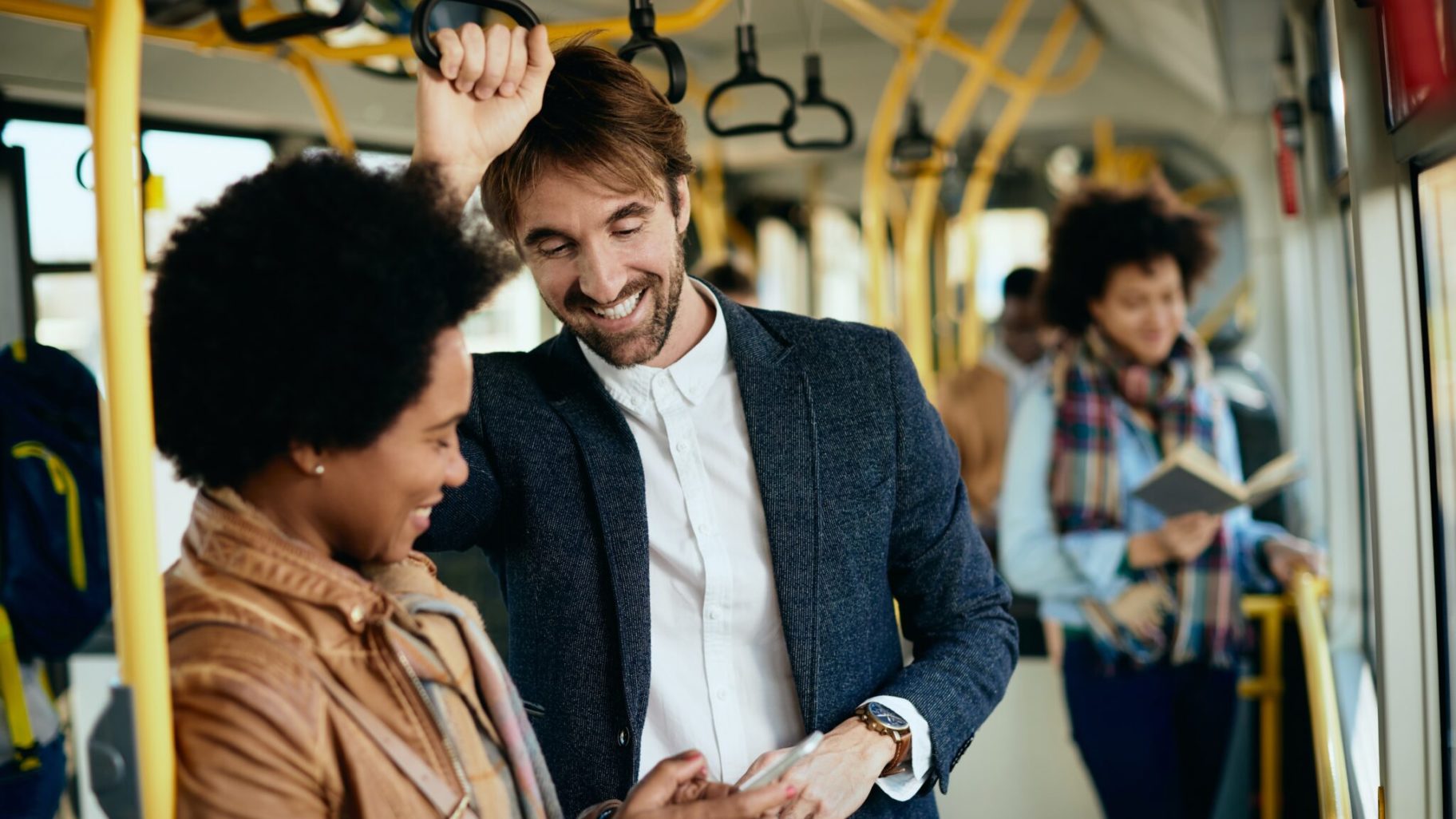 Two people laughing while looking at their phone inside a metro wagon