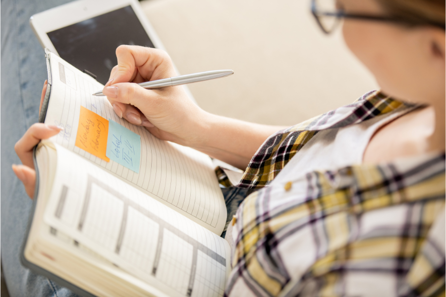 Person writing notes in a notebook with a pen, focusing on a desk workspace