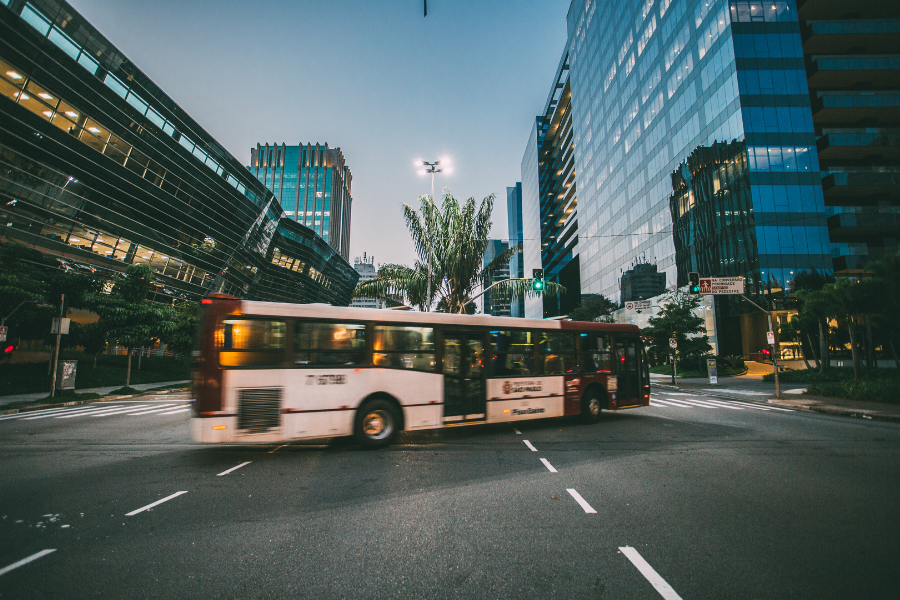 City street with a bus in motion, surrounded by urban buildings and traffic.