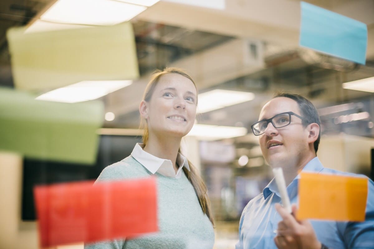Two professionals looking out through a large office window in a modern workplace setting.
