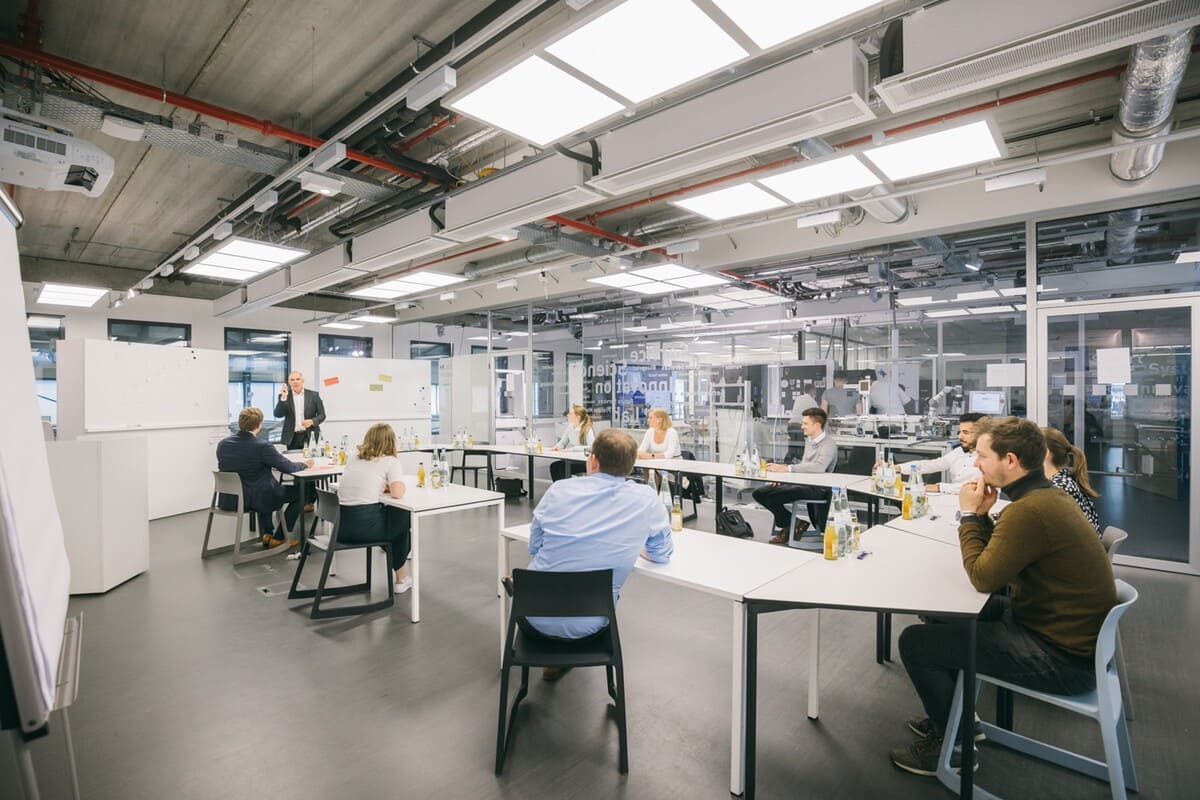 Modern office meeting room with a large table surrounded by chairs. The space is clean and professional, featuring natural lighting, minimal decor, and a collaborative workspace setup.
