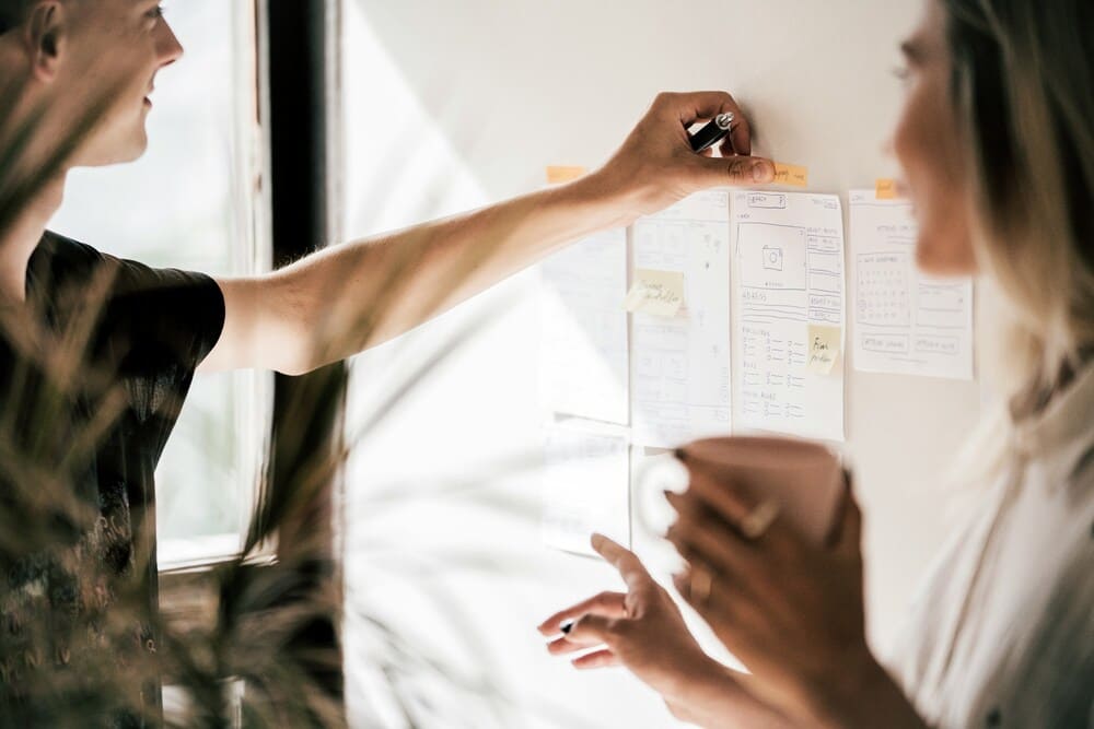 Two people attaching a paper to an office bulletin board.