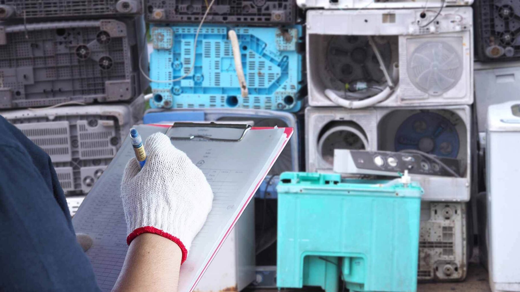 a person holding a clipboard in front of a pile of washing machines